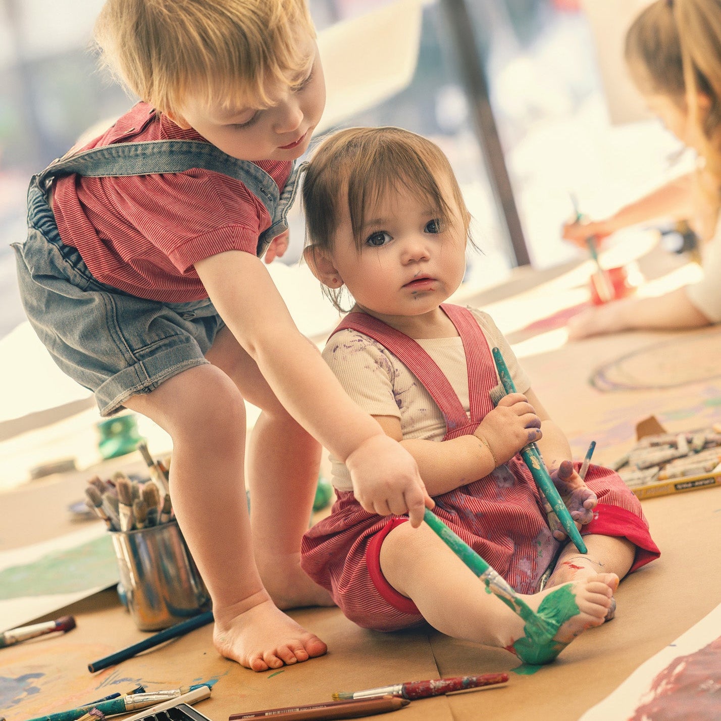 Two children with pinstripe romper playing with art supplies on a table.